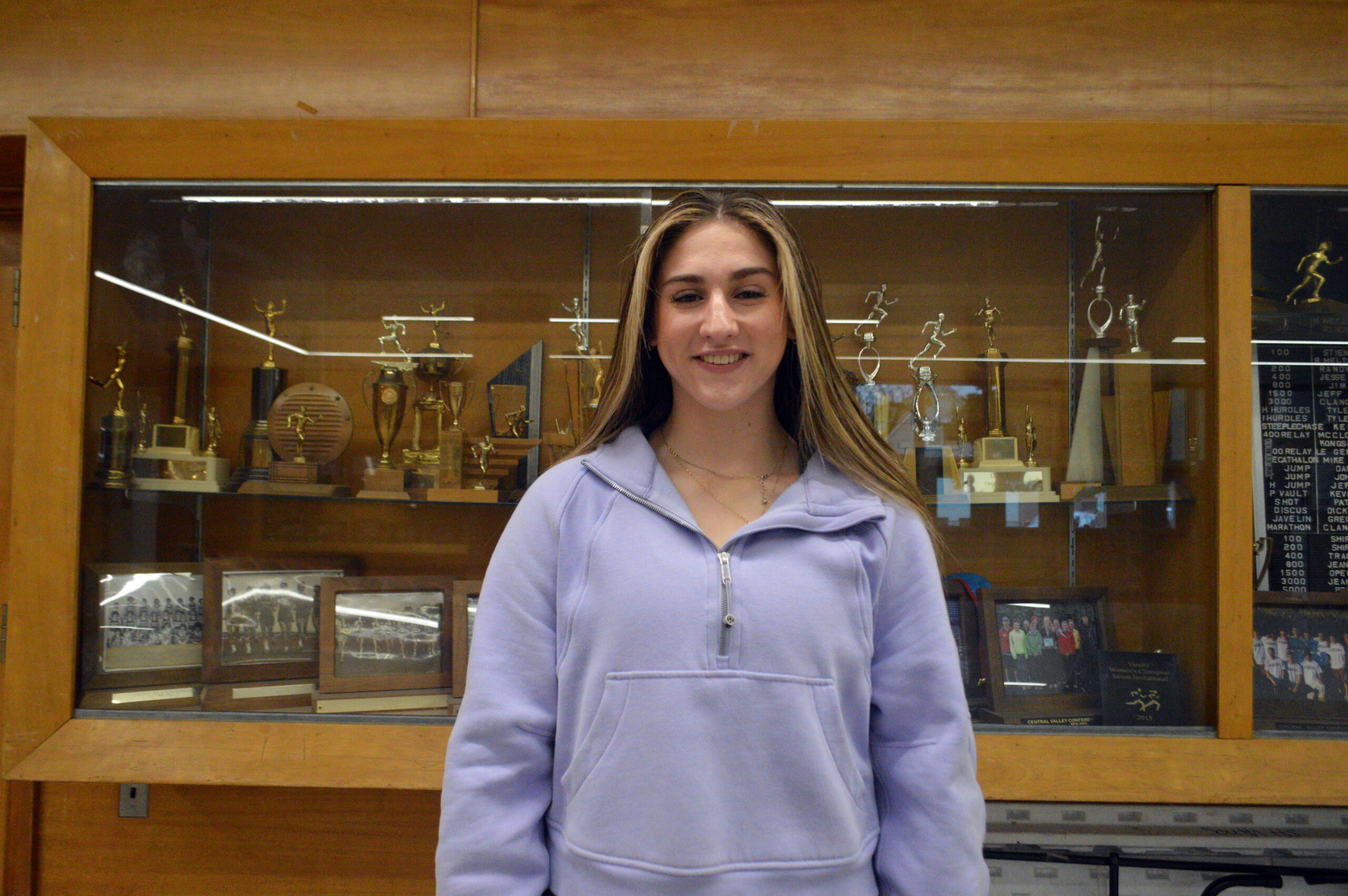Photo of Rowan Thompson in front of trophy case. Photo taken by Stephanie Romeo.