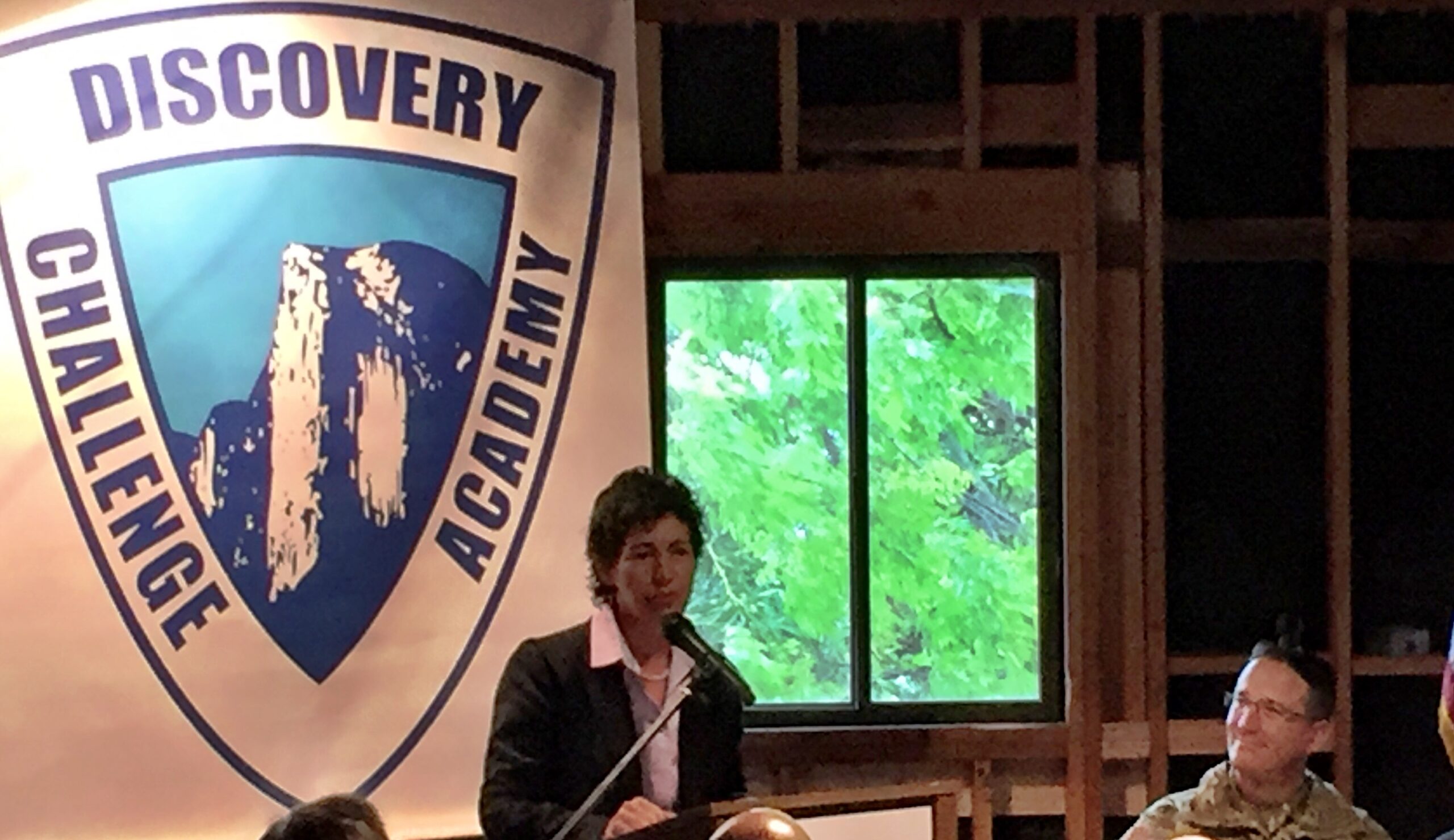 A woman presenting to a panel regarding Discovery High Schools.