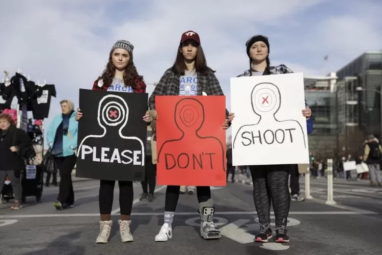 Three women hold signs up during a gun violence protest. The signs spell out "Please Don't Shoot."